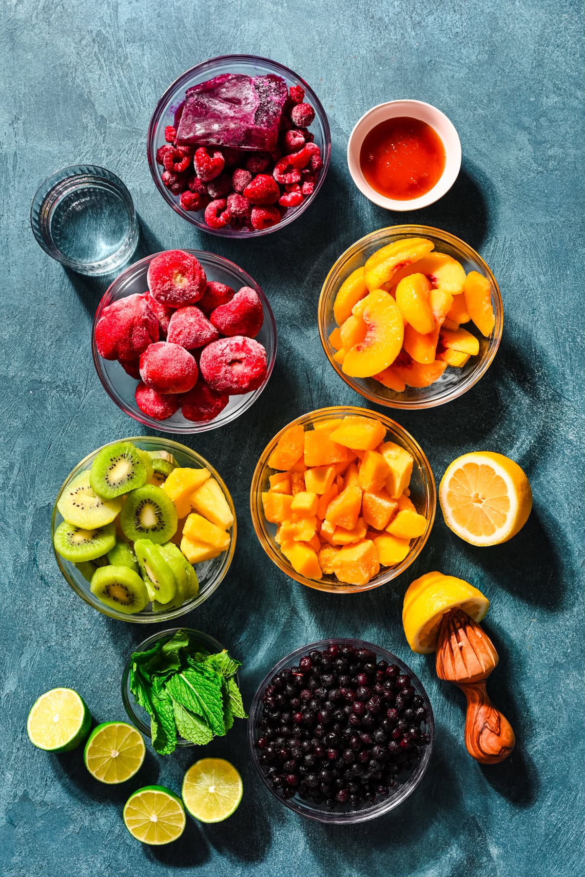 Overhead view of homemade freeze pop ingredients, including frozen fruit, limes and lemons, and honey.