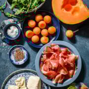 Overhead view of prosciutto melon salad ingredients, including cantaloupe and burrata.