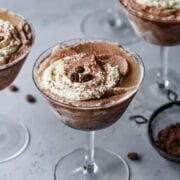 Rich chocolate mousse in cocktail glasses topped with whipped cream and coffee beans.