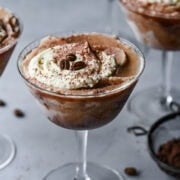 Rich coffee dessert topped with whipped cream, cocoa powder, and coffee beans in a martini glass.