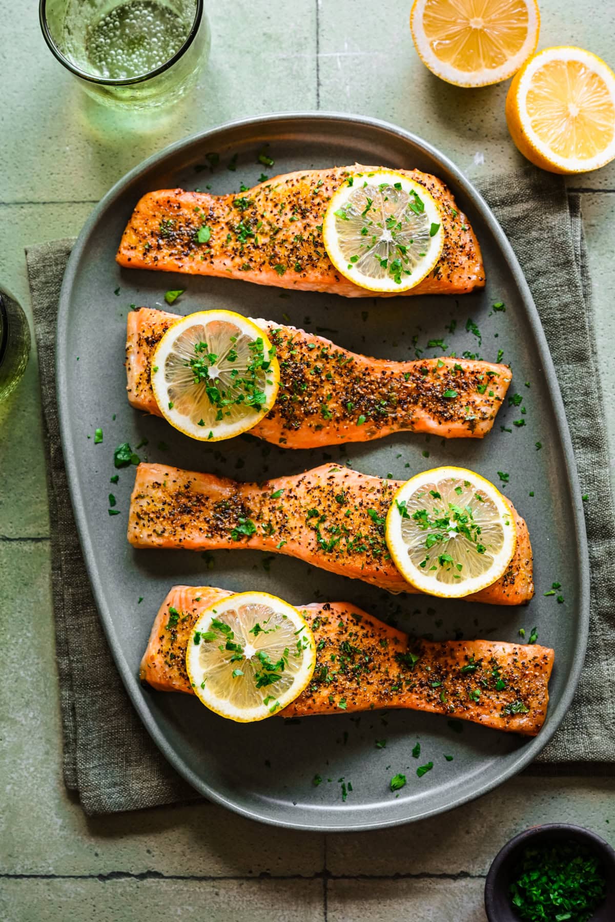 Overhead view of lemon pepper salmon on green platter with lemon slices as garnish.