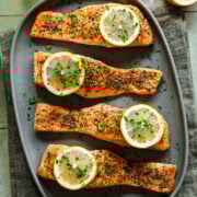 Overhead view of lemon pepper salmon on green platter with lemon slices as garnish.