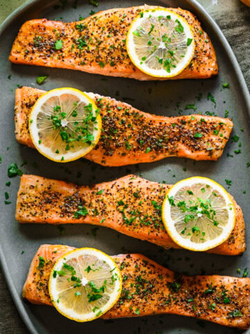 Overhead view of lemon pepper salmon on green platter with lemon slices as garnish.