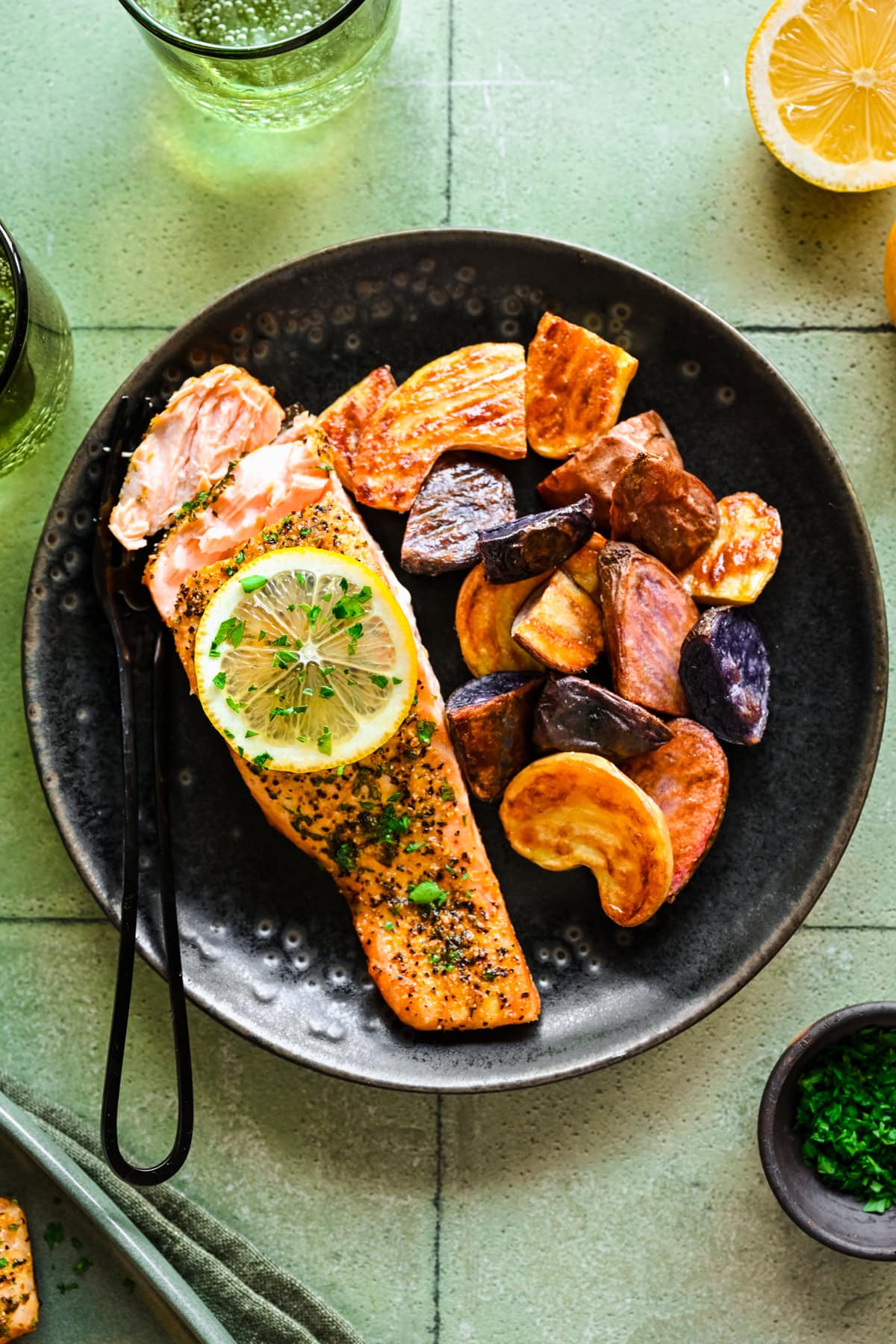 overhead view of lemon pepper salmon on a black plate with roasted potatoes.