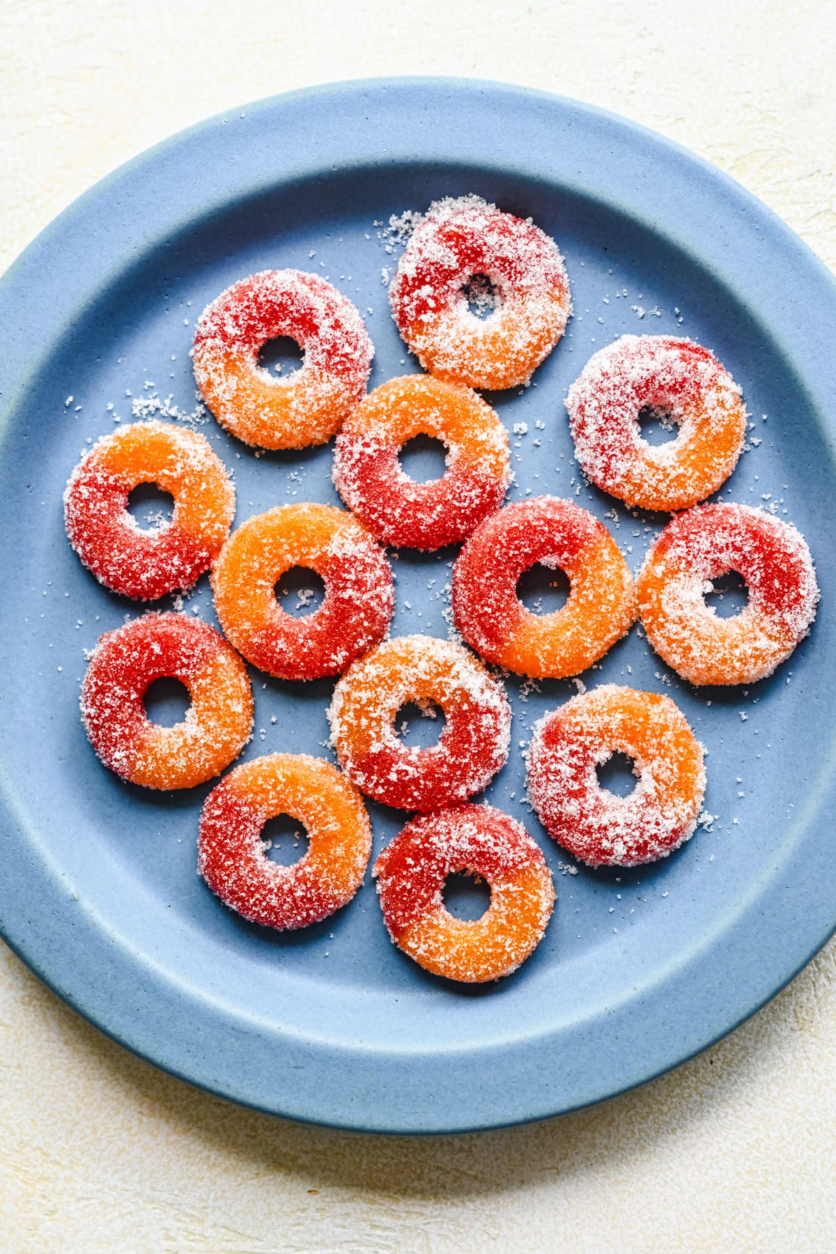 Overhead view of peach rings covered in sugar on a blue plate.