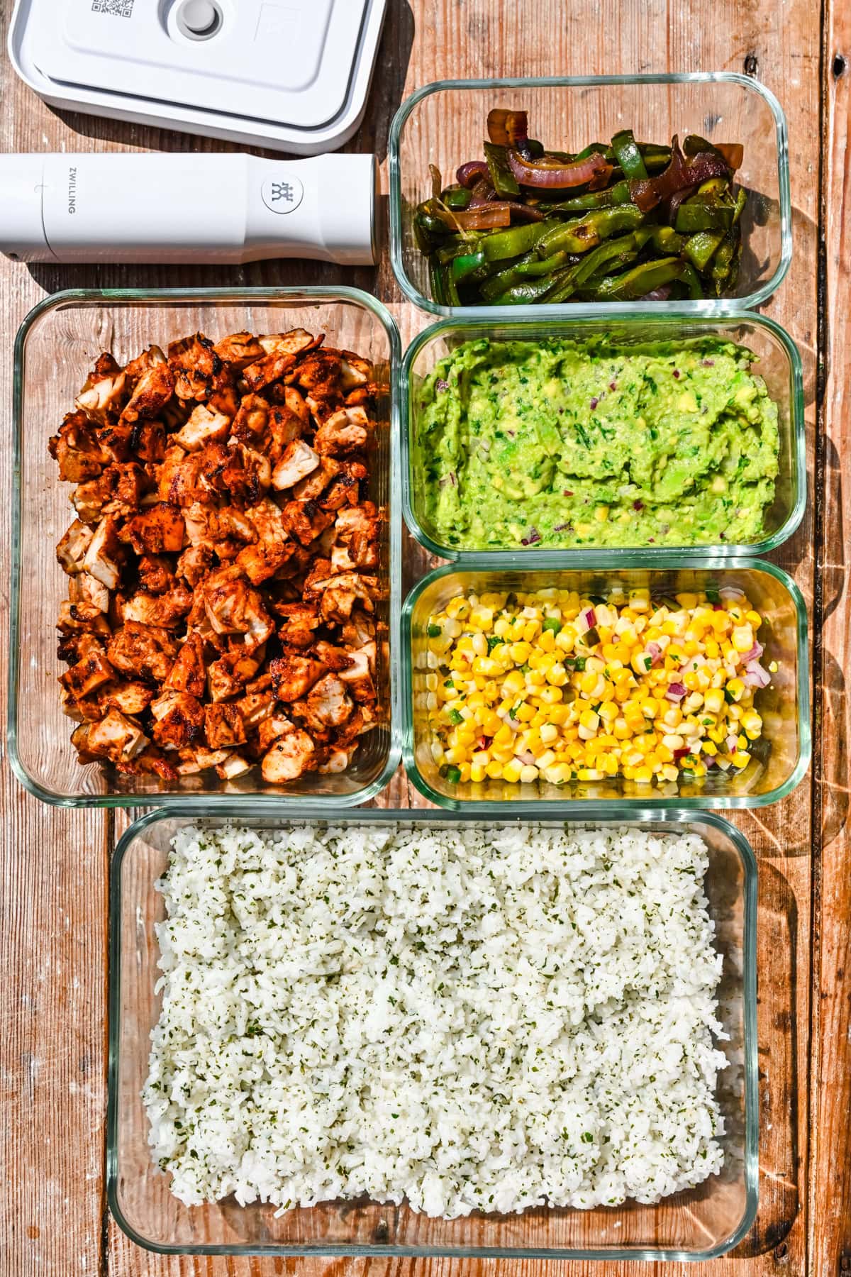 Overhead view of veggies, chicken, guacamole, corn, and rice in storage containers.