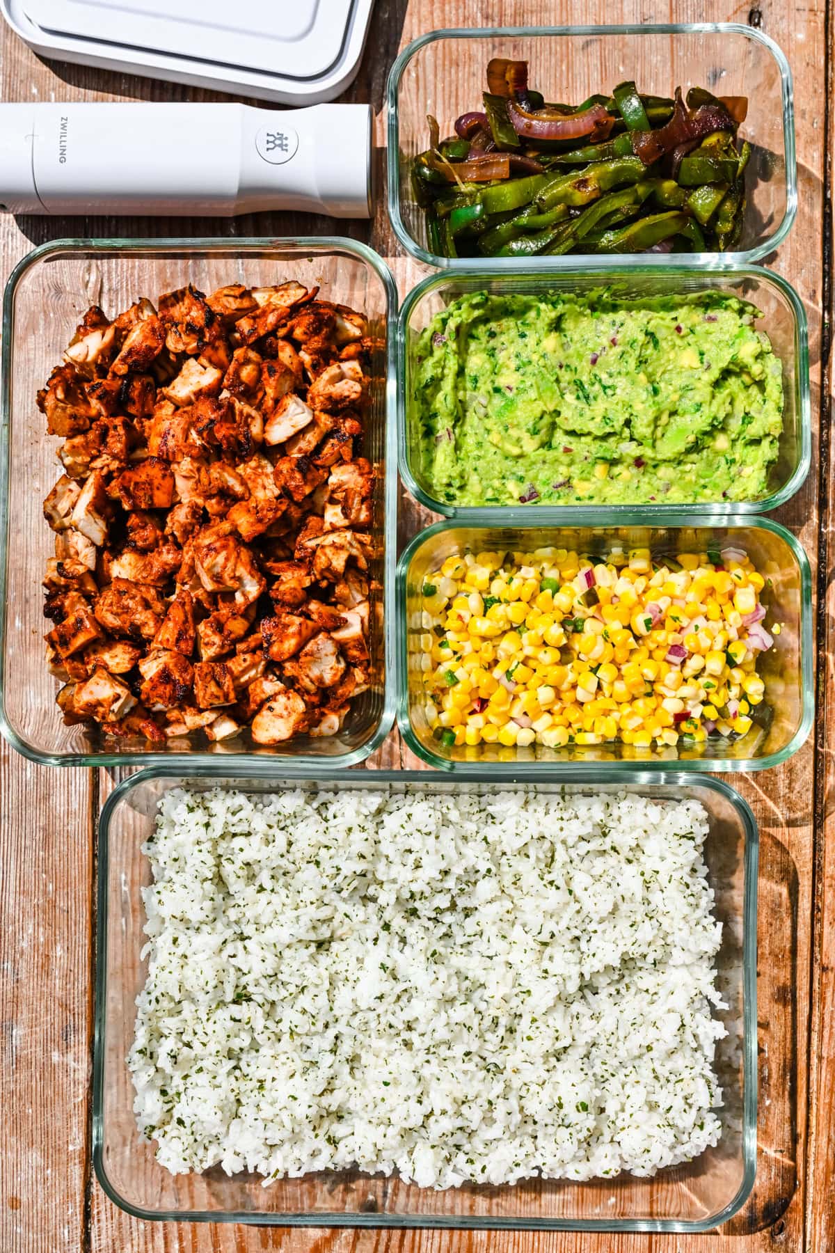 Overhead view of veggies, chicken, guacamole, corn, and rice in storage containers.