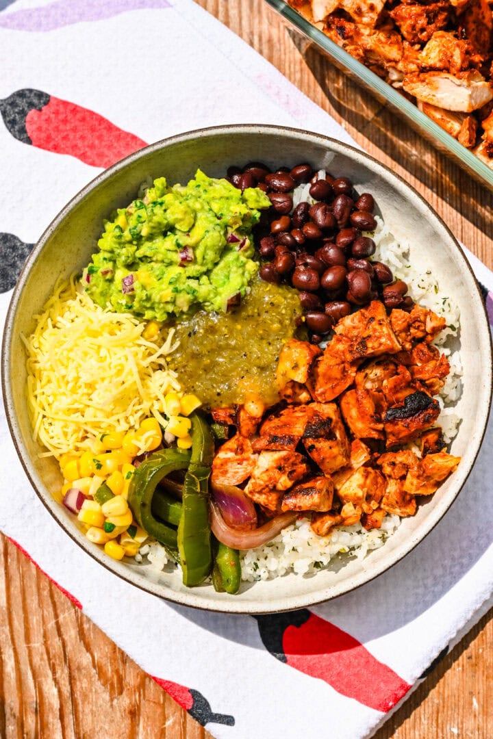Overhead view of burrito bowl with chicken veggies guacamole cheese and beans.
