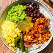 Overhead view of burrito bowl with chicken veggies guacamole cheese and beans.