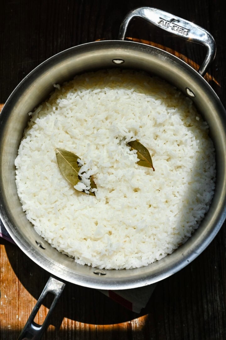 Overhead view of rice in a pot with bay leaves.