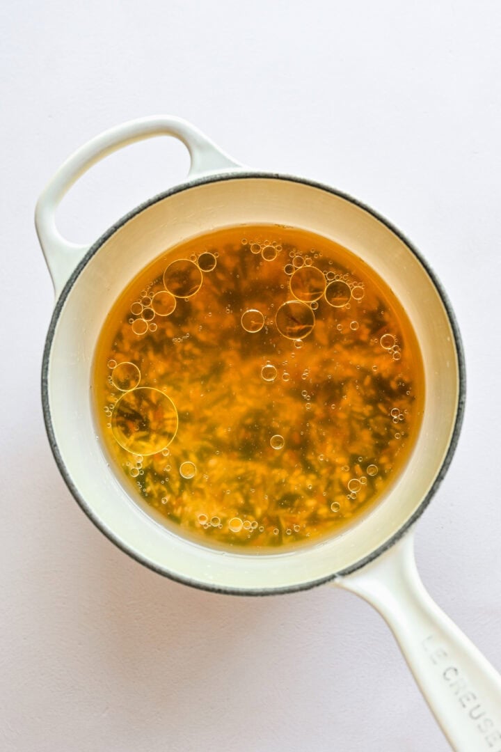 Uncooked rice in a pot with broth.