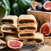 Chocolate fig cookies on wire rack with fresh figs and green plants in background.