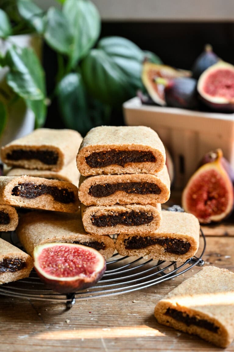 Chocolate fig cookies on wire rack with fresh figs and green plants in background.