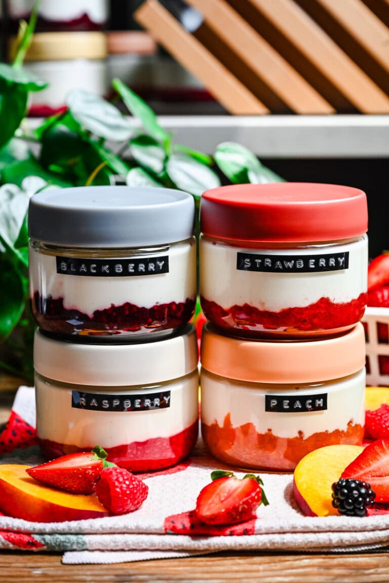 Freshly made berry and peach desserts in glass jars with colorful lids, surrounded by fresh fruit.
