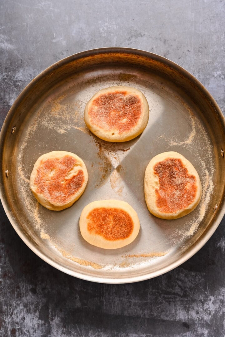 Four english muffins cooking in a pan.