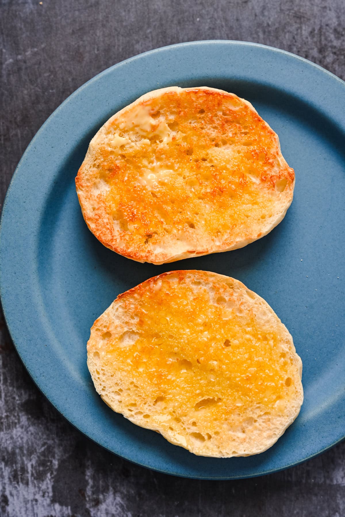 Overhead view of an english muffin cut in half with butter spread on it.