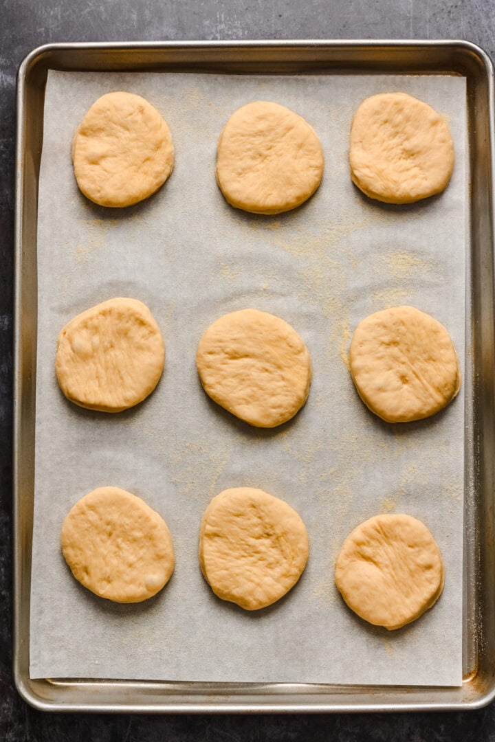 English muffins cut out and resting on parchment paper.