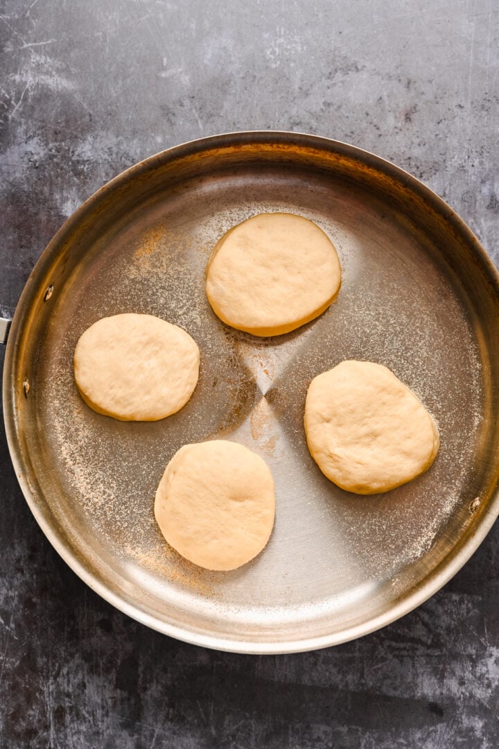 Four english muffins cooking in a pan.