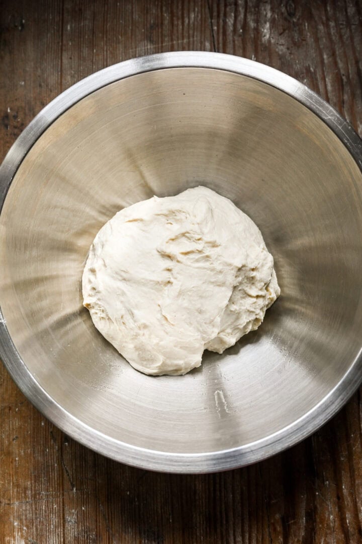 Overhead view of pizza dough in a stainless steel bowl.