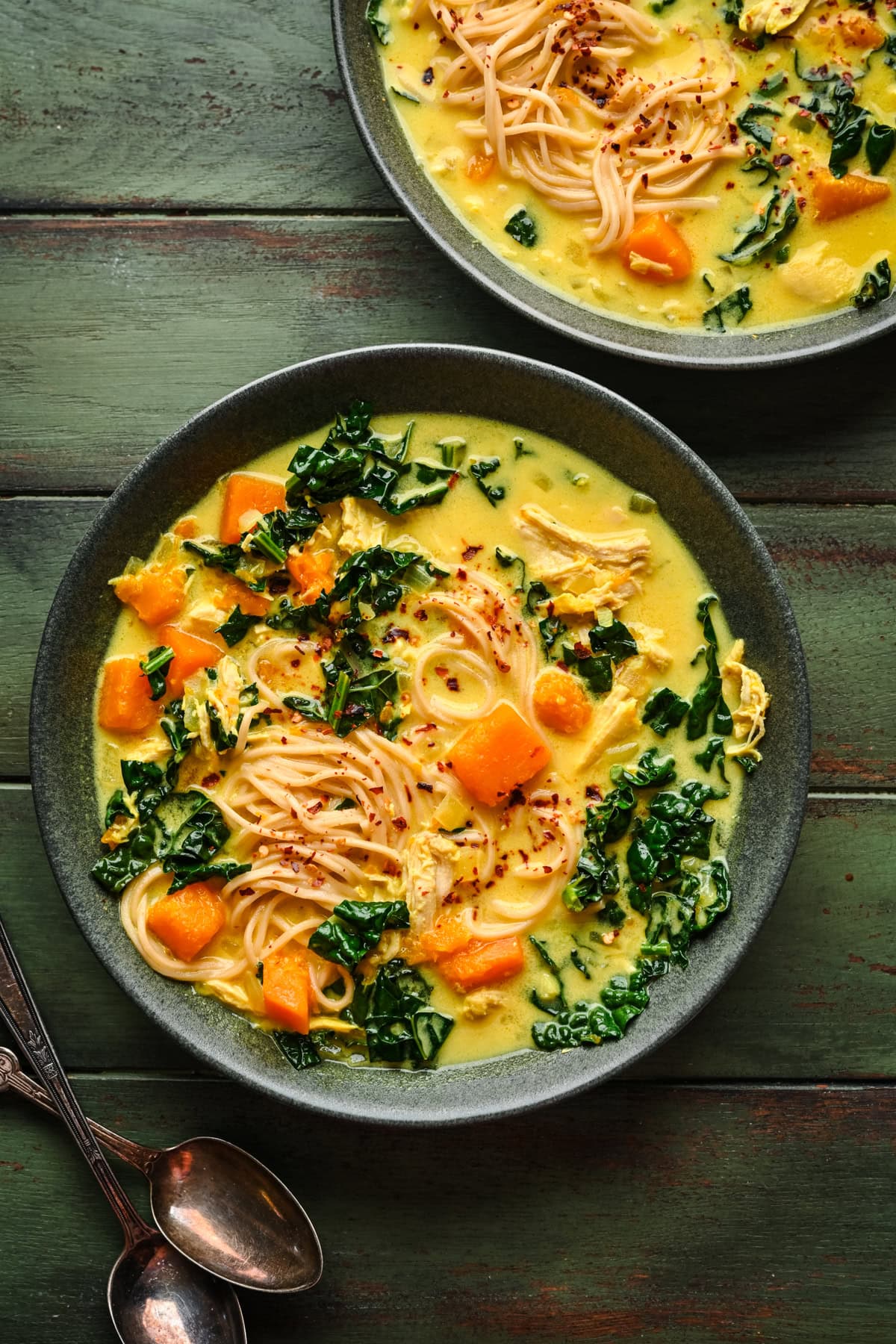 Soup in a bowl with noodles, butternut squash, and kale.