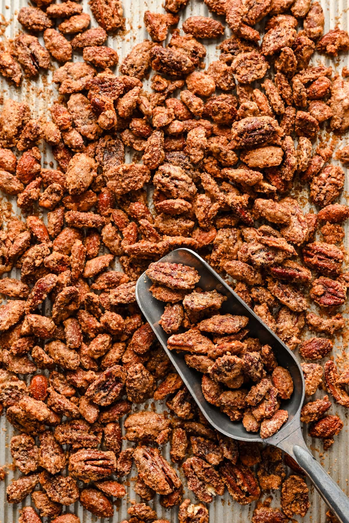 Overhead view of candied nuts on a sheet pan with a scooper.