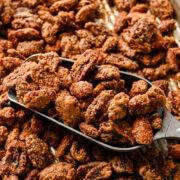 Overhead view of candied nuts on a sheet pan with a scooper.