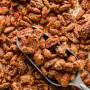 Crunchy candied pecans scattered on a baking sheet with a metal scoop.