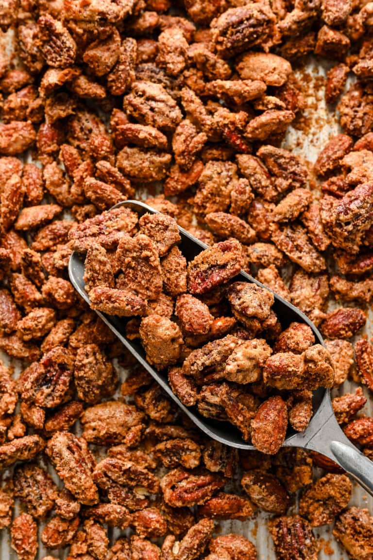 Crunchy candied pecans scattered on a baking sheet with a metal scoop.