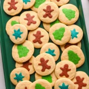 Colorful sugar cookies decorated with gingerbread men, stars, and state-shaped designs on a green tray.