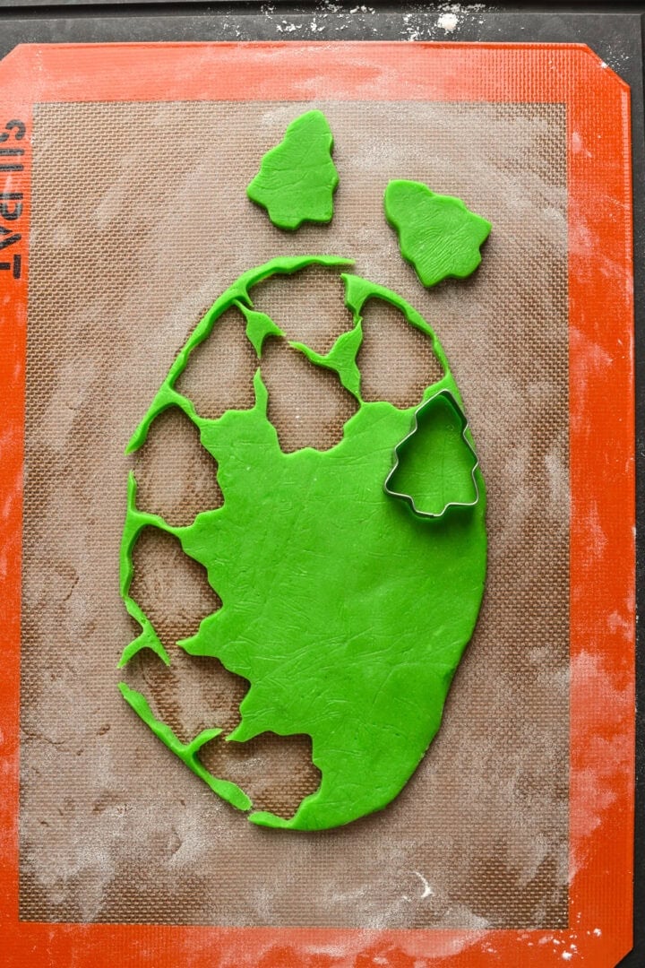 Flat sheet of dough with green christmas trees cut out of it.