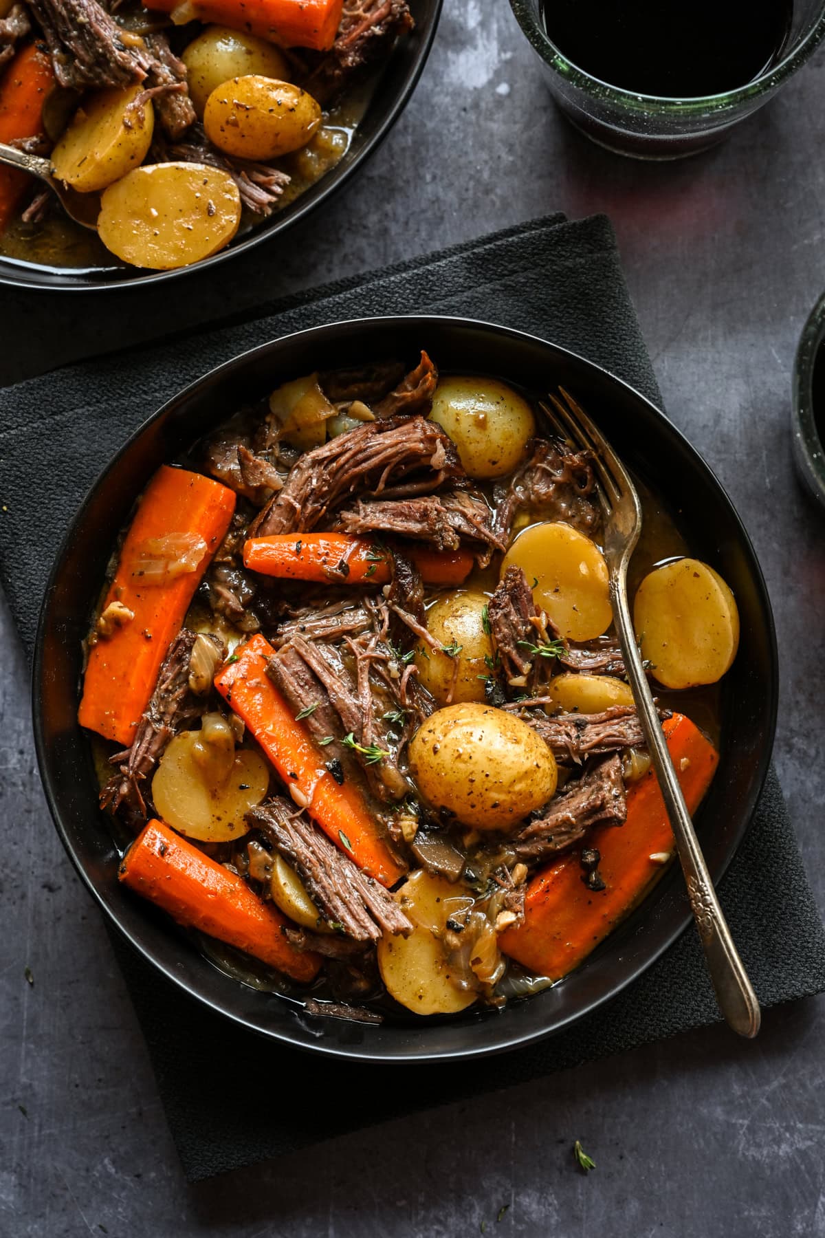 Overhead view of pot roast with potatoes and carrots in a black bowl.