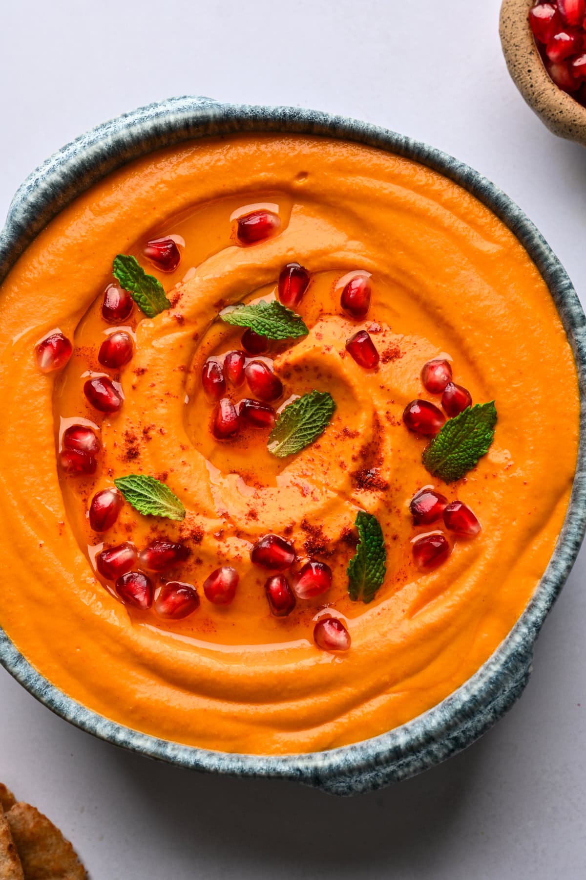 Overhead view of carrot and roasted red pepper dip garnished with pomegranate and mint. 