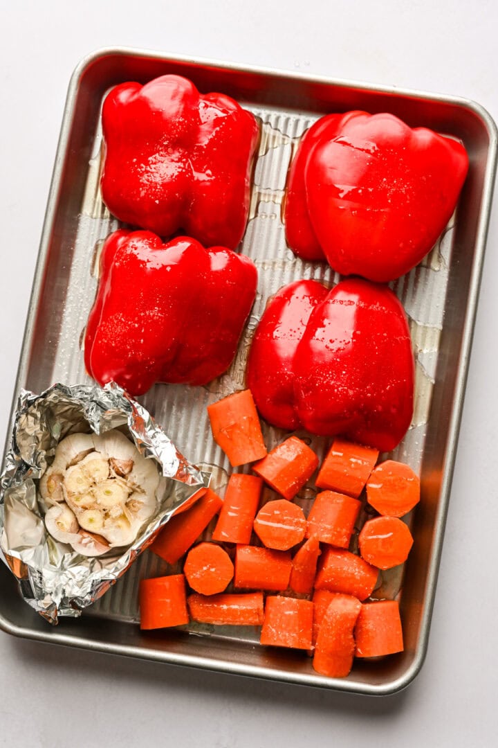 Red peppers, carrots and garlic on a sheet pan before roasting. 