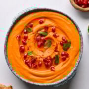 Creamy roasted carrot hummus garnished with pomegranate seeds and mint, served with pita bread, healthy snack, dip, vegetable, vegan, gluten-free, made from scratch.