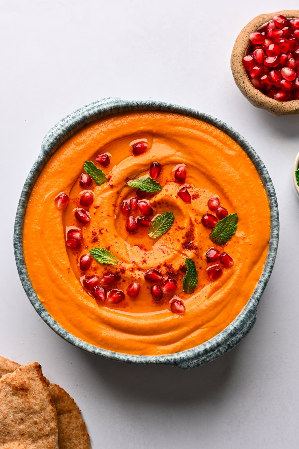 Overhead view of carrot and roasted red pepper dip garnished with pomegranate and mint.