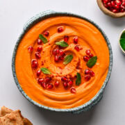 Overhead view of carrot and roasted red pepper dip garnished with pomegranate and mint.