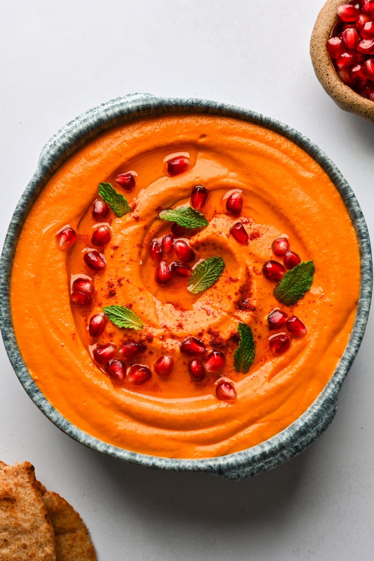 Overhead view of carrot and roasted red pepper feta dip garnished with pomegranate and mint.