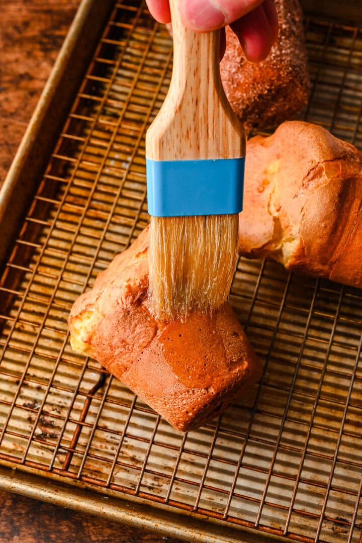 Brushing cooled popover with butter.