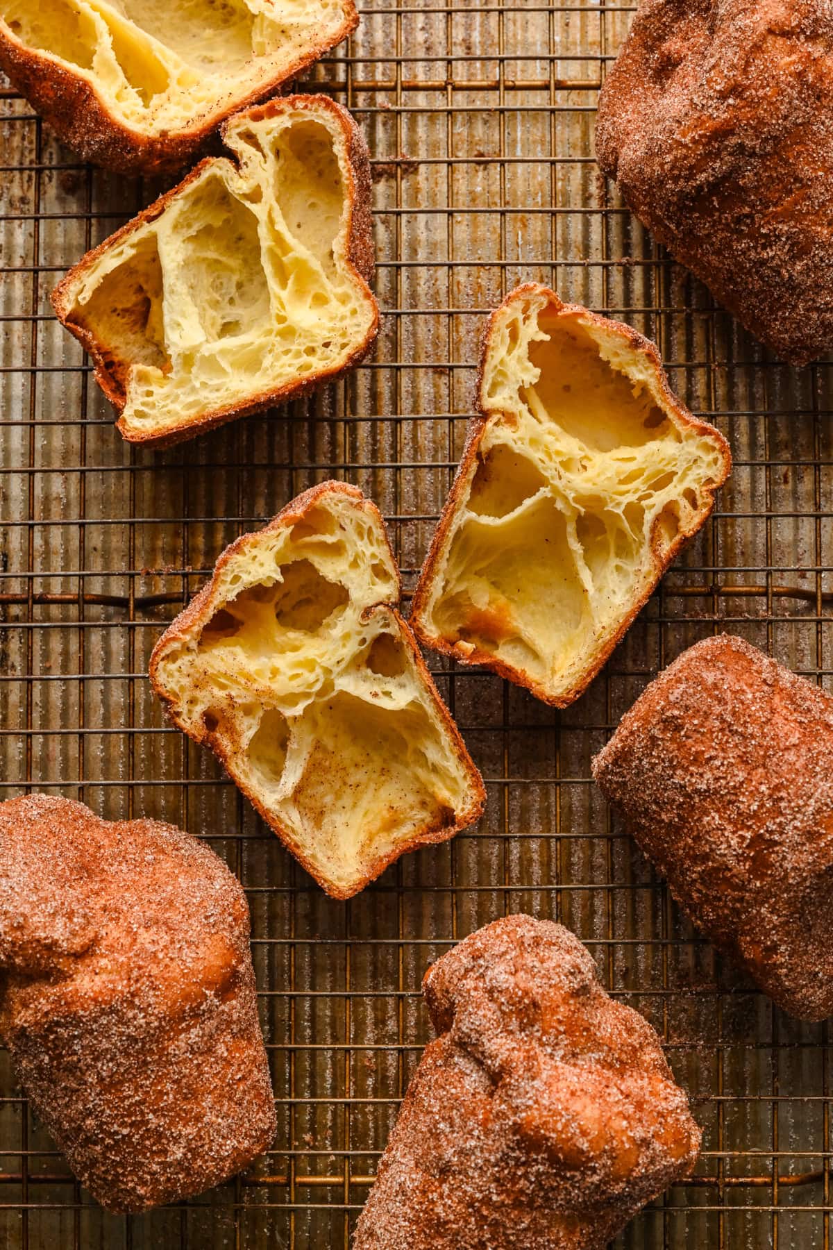 Overhead view of cinnamon sugar popovers on cooling rack with one cut open to show inside. 