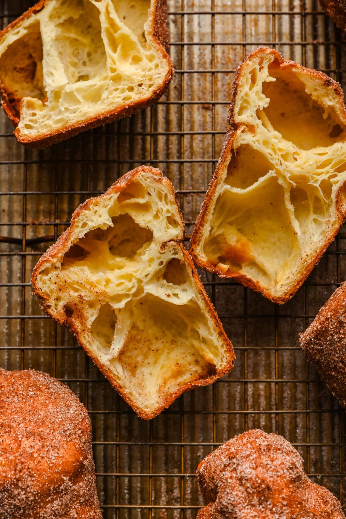Overhead view of cinnamon sugar popovers on cooling rack with one cut open to show inside. 