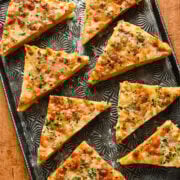 Cheese pizza slices on a decorative black platter, garnished with herbs.