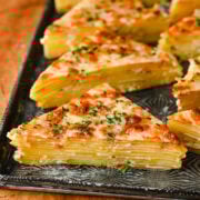 Buttered potato gratin slices with cheese and herbs on a black tray.