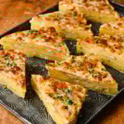 Rich, cheesy baked pasta slices garnished with herbs on a black serving tray.