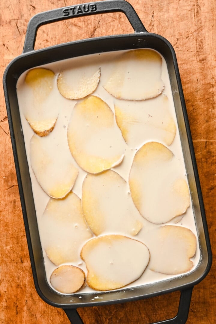 Layered potatoes covered with cream in a roasting pan.