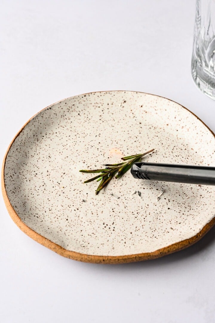 lighting a piece of rosemary on fire on a plate.