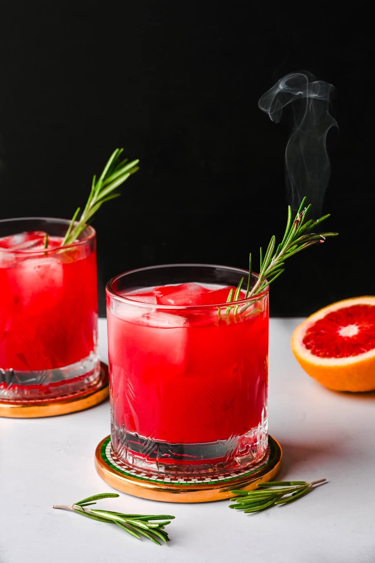 Side view of blood orange fireside cocktail garnished with a smoking rosemary sprig.