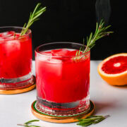 Side view of blood orange fireside cocktail garnished with a smoking rosemary sprig.