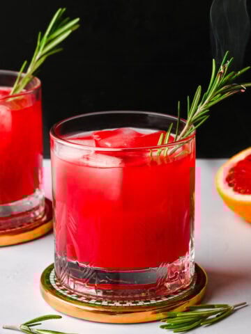 Side view of blood orange fireside cocktail garnished with a smoking rosemary sprig.