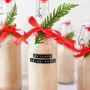 Cream-filled bottles decorated with red ribbons and greenery, perfect for festive holiday party decor.