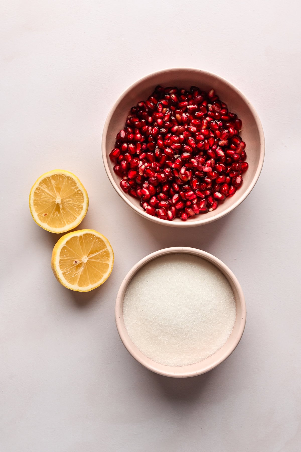Overhead view of bowl of pomegranate arils, sugar and lemon.